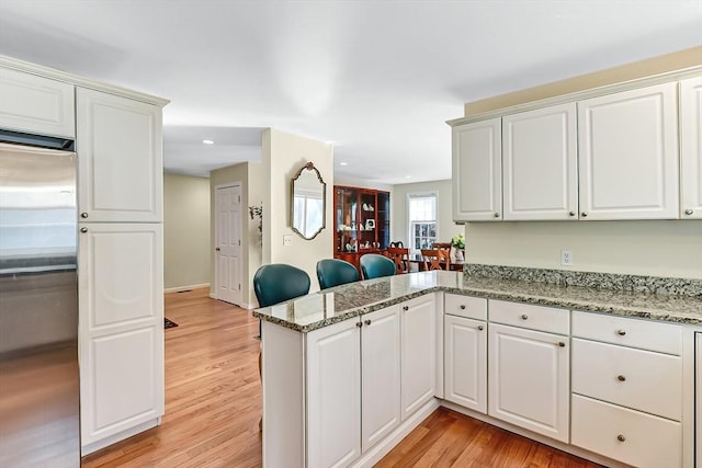 kitchen with white cabinetry, light stone countertops, kitchen peninsula, and stainless steel refrigerator