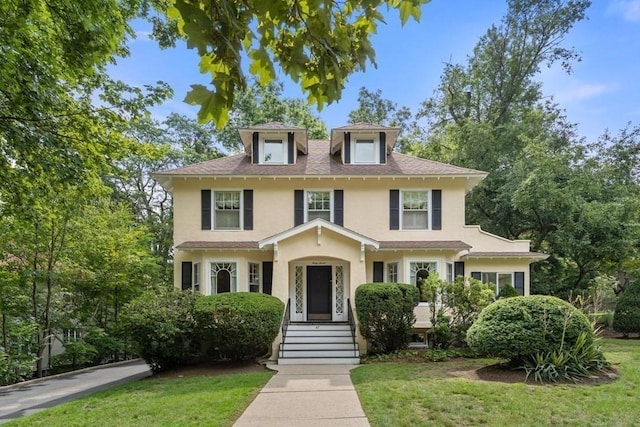 american foursquare style home featuring a shingled roof, a front lawn, and stucco siding