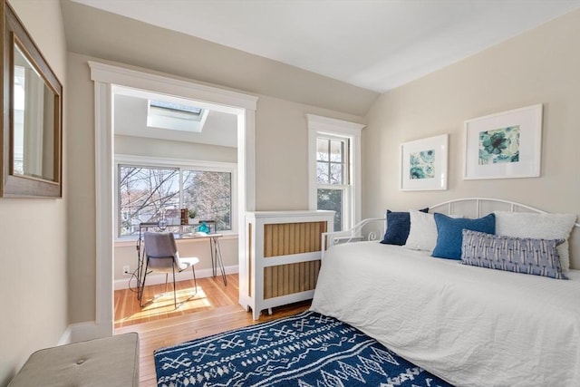 bedroom with vaulted ceiling with skylight, hardwood / wood-style floors, and baseboards