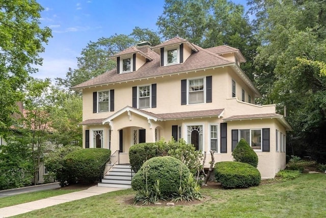 american foursquare style home featuring a shingled roof, a front yard, and stucco siding