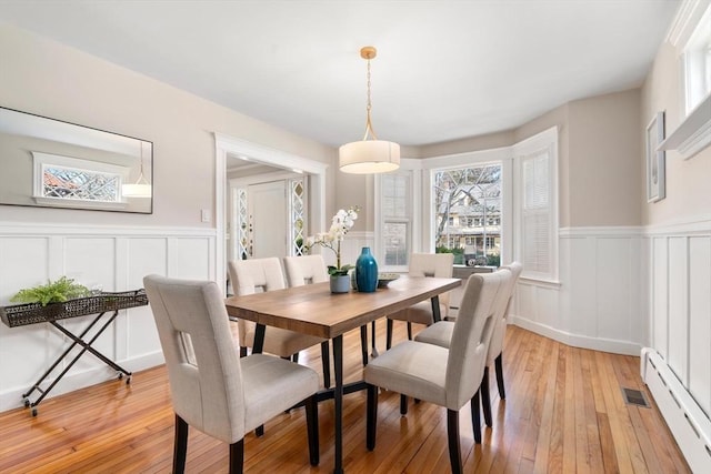 dining space featuring a baseboard heating unit, a wainscoted wall, and light wood-style floors