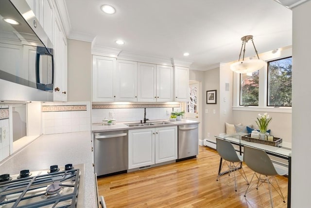 kitchen with white cabinets, appliances with stainless steel finishes, ornamental molding, light countertops, and a sink