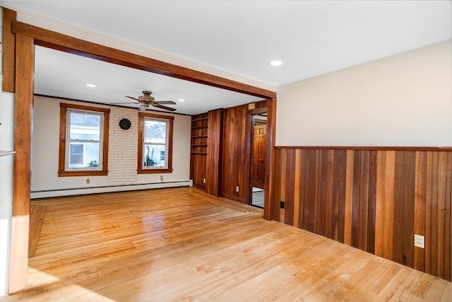 spare room featuring baseboard heating, ceiling fan, light hardwood / wood-style flooring, and wood walls