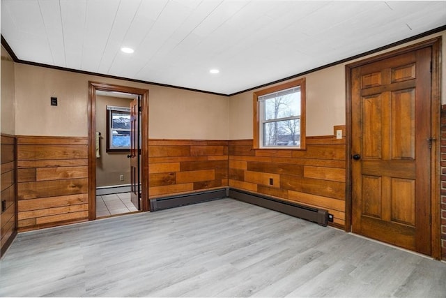 empty room featuring crown molding, a wealth of natural light, light hardwood / wood-style flooring, and wood walls