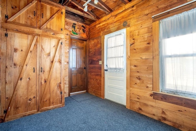 doorway to outside with vaulted ceiling with beams, wood walls, dark colored carpet, and wooden ceiling