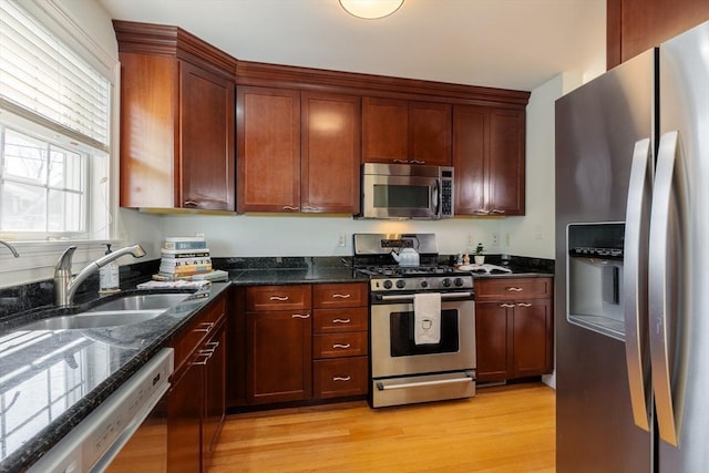 kitchen with appliances with stainless steel finishes, dark stone counters, a sink, and light wood finished floors