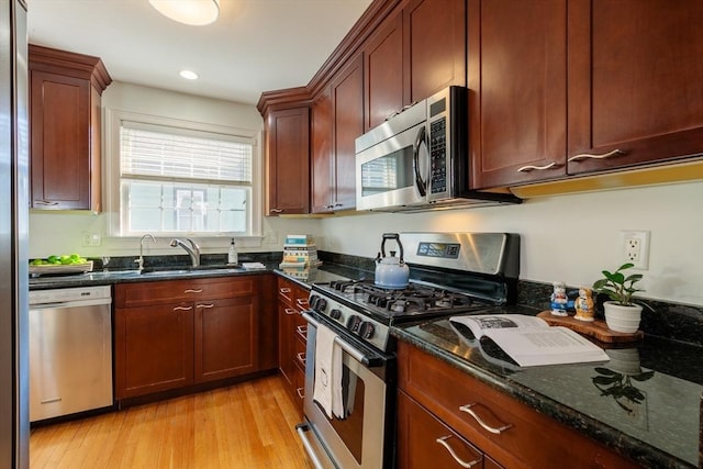 kitchen featuring light wood-style flooring, appliances with stainless steel finishes, dark stone countertops, a sink, and recessed lighting