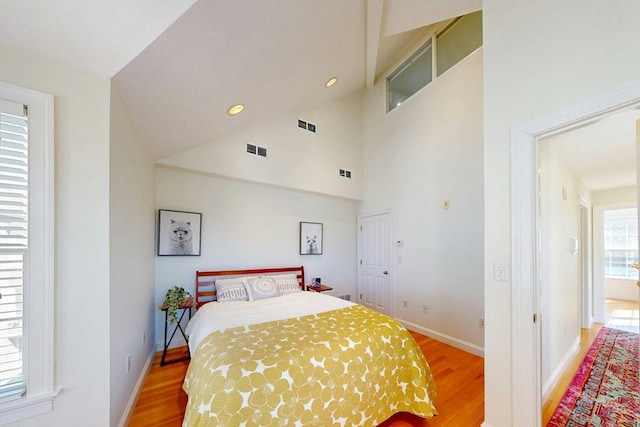 bedroom featuring baseboards, high vaulted ceiling, visible vents, and light wood-style floors