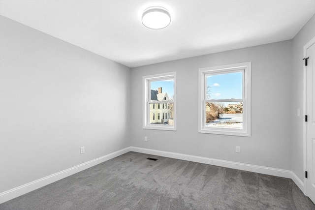 spare room with visible vents, baseboards, and dark colored carpet