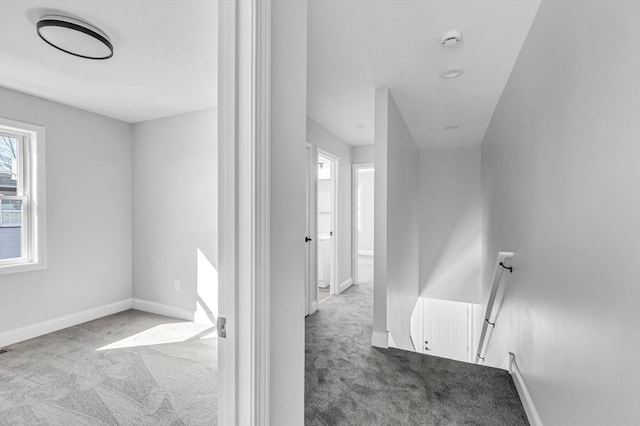 corridor with carpet, baseboards, and an upstairs landing