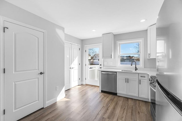 kitchen featuring wood finished floors, light countertops, stainless steel appliances, white cabinetry, and a sink