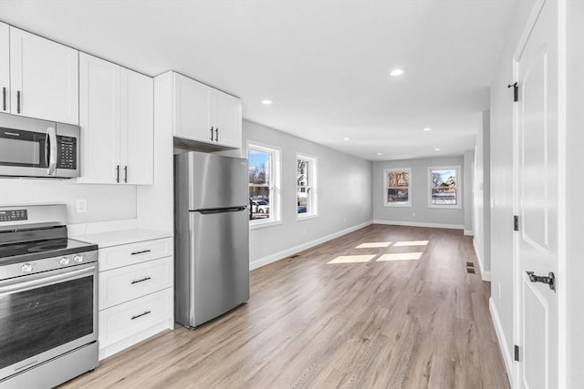 kitchen featuring light wood-type flooring, a healthy amount of sunlight, appliances with stainless steel finishes, and white cabinets