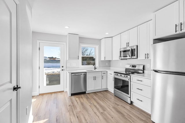 kitchen featuring light wood finished floors, stainless steel appliances, light countertops, white cabinetry, and a sink