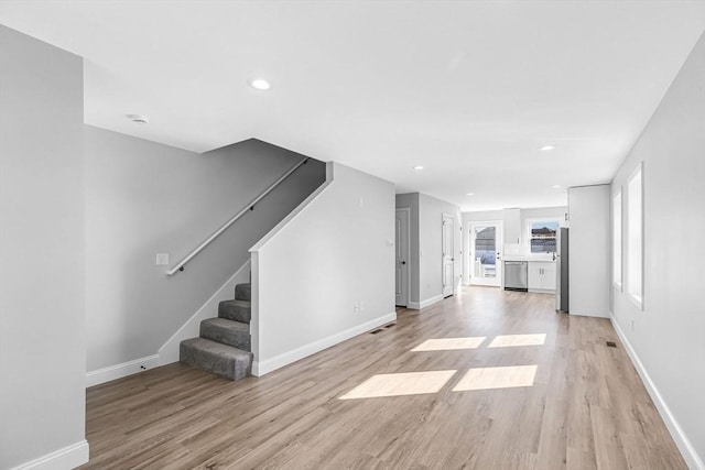 unfurnished living room featuring light wood finished floors, baseboards, stairway, and recessed lighting