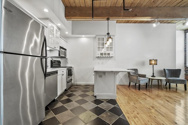 kitchen with beamed ceiling, appliances with stainless steel finishes, white cabinetry, and pendant lighting