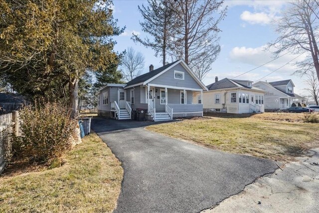 view of front facade with a front lawn, a chimney, covered porch, and driveway