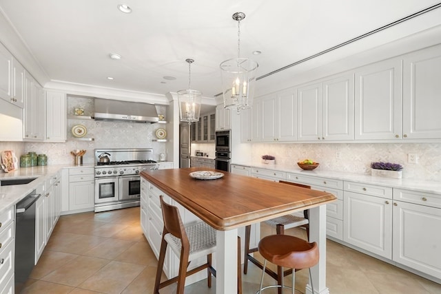 kitchen with wall chimney range hood, tasteful backsplash, white cabinetry, appliances with stainless steel finishes, and light tile patterned flooring