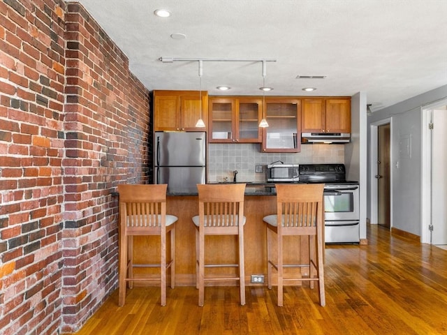 kitchen with appliances with stainless steel finishes, a kitchen breakfast bar, tasteful backsplash, and dark wood-type flooring