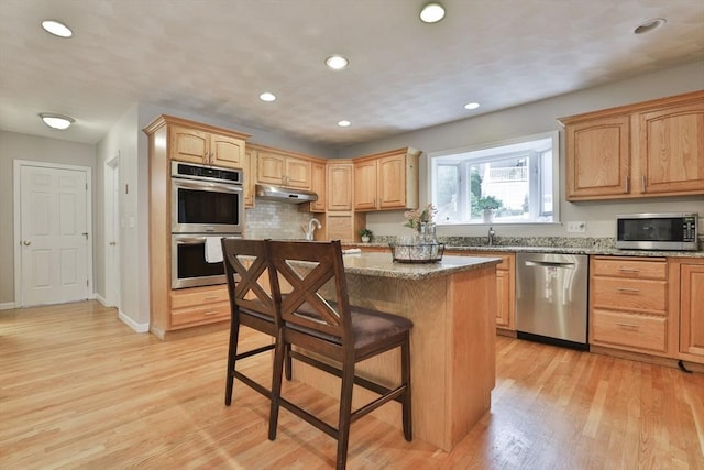 kitchen with a kitchen breakfast bar, a center island, under cabinet range hood, stainless steel appliances, and light wood-style flooring