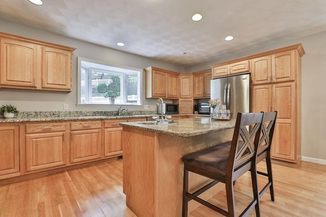 kitchen featuring freestanding refrigerator, light stone countertops, a breakfast bar area, recessed lighting, and light wood-type flooring