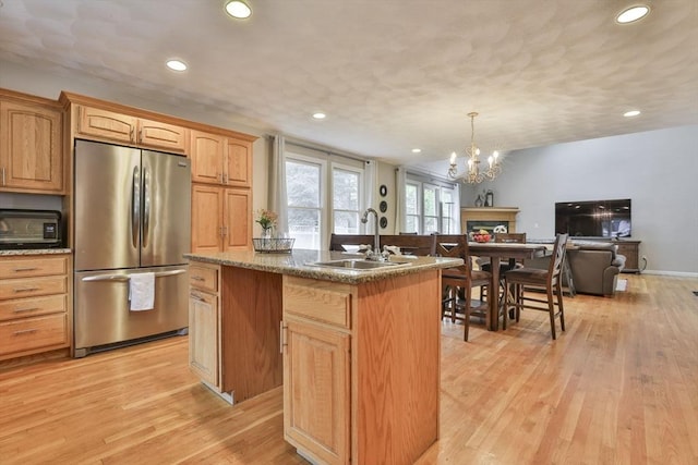 kitchen with freestanding refrigerator, light wood-style floors, open floor plan, an island with sink, and a sink