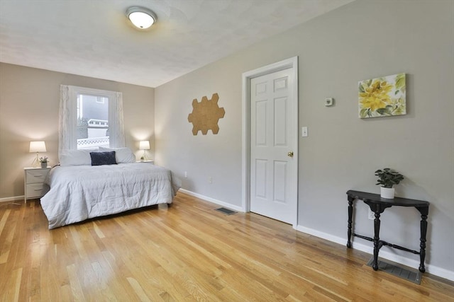 bedroom with baseboards, light wood finished floors, and visible vents