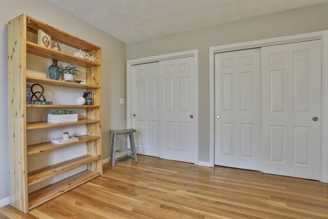 bedroom featuring baseboards, multiple closets, and light wood-style flooring