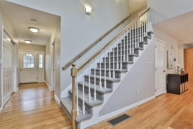 foyer with stairway, baseboards, wood finished floors, and visible vents