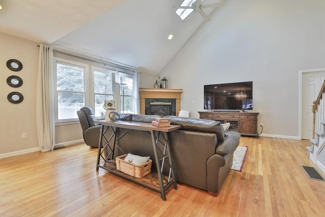 living area with visible vents, a fireplace, high vaulted ceiling, a ceiling fan, and light wood-style flooring