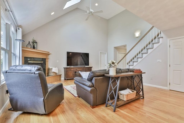 living area with stairs, a fireplace, ceiling fan, high vaulted ceiling, and light wood-style flooring