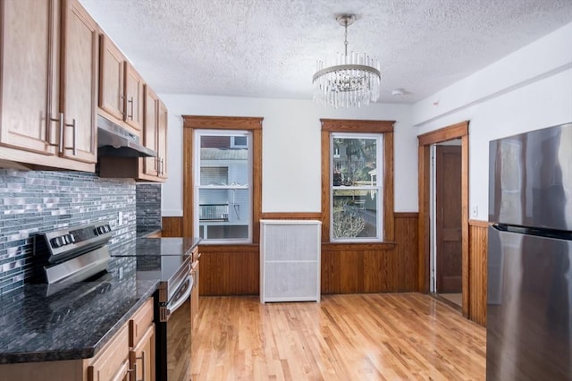 kitchen featuring pendant lighting, an inviting chandelier, light hardwood / wood-style flooring, dark stone countertops, and stainless steel appliances