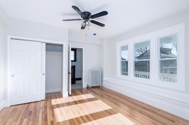 unfurnished bedroom with ceiling fan, light hardwood / wood-style floors, radiator, and multiple windows