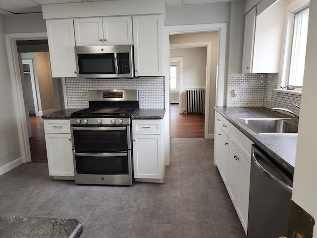 235 Common St, Watertown, MA 02472 - kitchen featuring stainless steel appliances, radiator heating unit, a sink, and white cabinetry