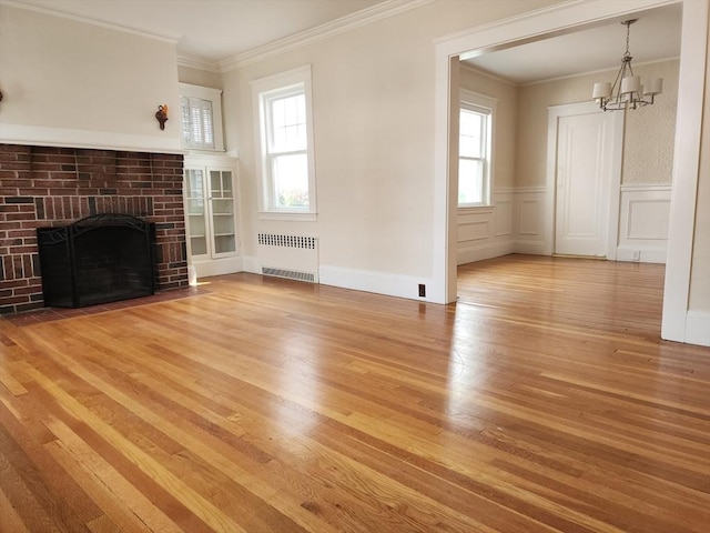 235 Common St, Watertown, MA 02472 - unfurnished living room with radiator, crown molding, wood finished floors, a chandelier, and a brick fireplace