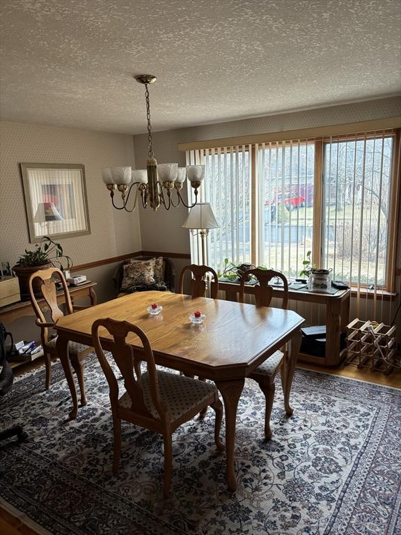 dining space featuring hardwood / wood-style flooring, a wealth of natural light, a textured ceiling, and a notable chandelier