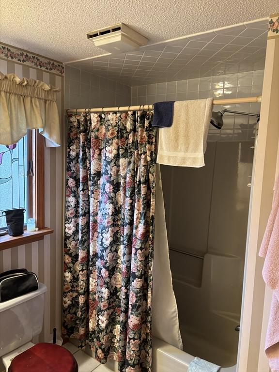 bathroom with a textured ceiling, shower / tub combo, and tile patterned flooring