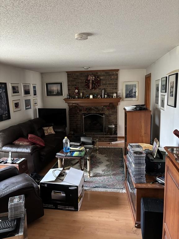 living room with a brick fireplace, a textured ceiling, and light hardwood / wood-style floors