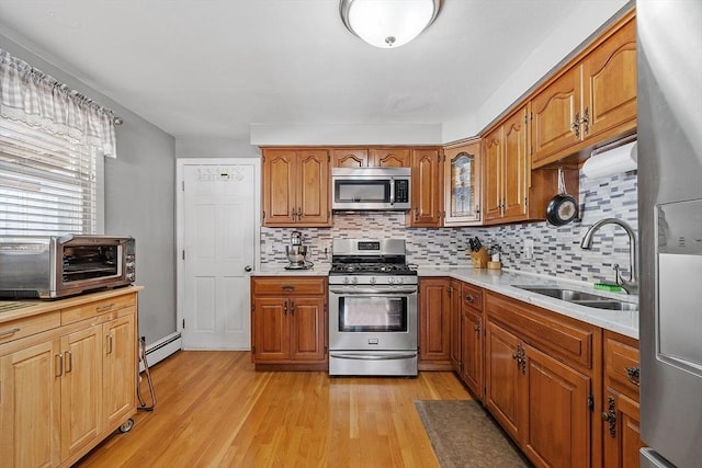 kitchen with sink, backsplash, baseboard heating, stainless steel appliances, and light wood-type flooring