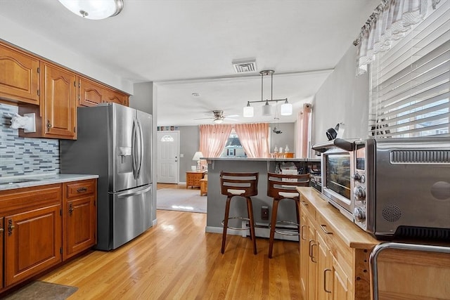 kitchen with hanging light fixtures, stainless steel fridge, ceiling fan, light hardwood / wood-style floors, and backsplash