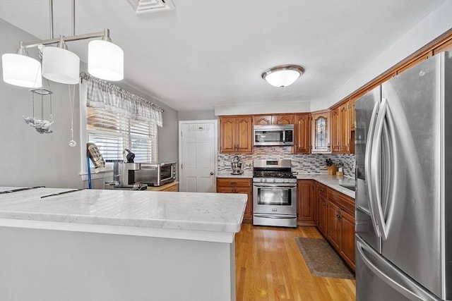 kitchen featuring stainless steel appliances, tasteful backsplash, light hardwood / wood-style flooring, and decorative light fixtures