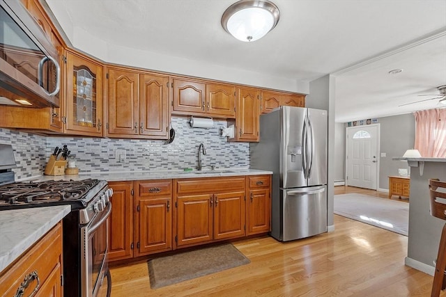 kitchen with appliances with stainless steel finishes, tasteful backsplash, sink, ceiling fan, and light hardwood / wood-style flooring