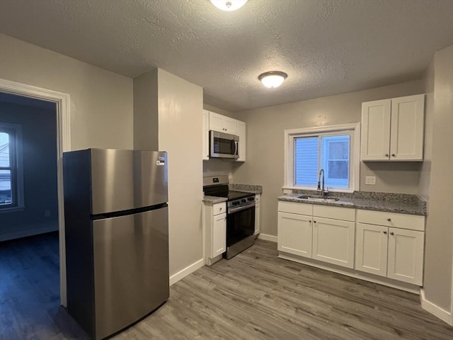 kitchen with white cabinetry, appliances with stainless steel finishes, a sink, and wood finished floors