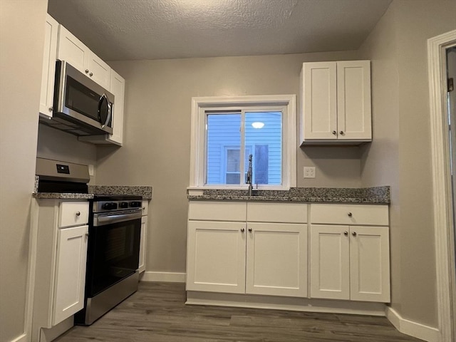 kitchen with dark wood finished floors, white cabinets, appliances with stainless steel finishes, a textured ceiling, and a sink