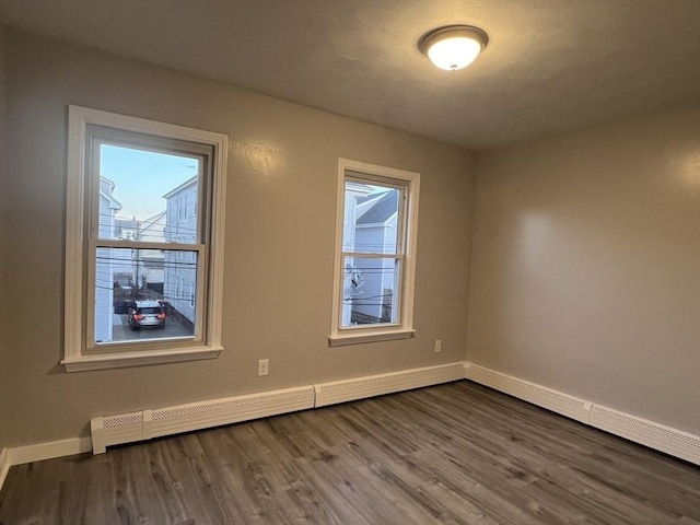 empty room with a baseboard radiator, baseboards, and wood finished floors