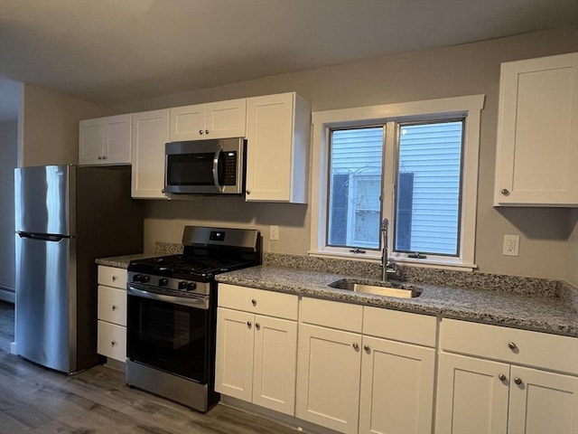 kitchen with dark wood-type flooring, appliances with stainless steel finishes, white cabinets, and a sink