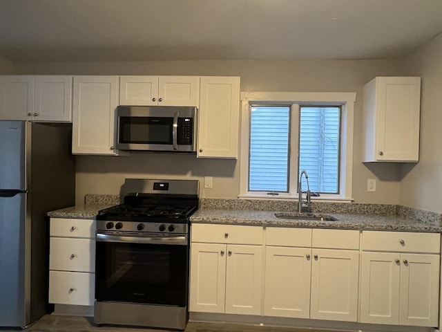 kitchen featuring light stone counters, appliances with stainless steel finishes, white cabinets, and a sink