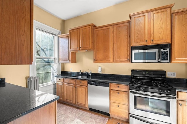 kitchen with stainless steel appliances, radiator heating unit, dark countertops, and a sink