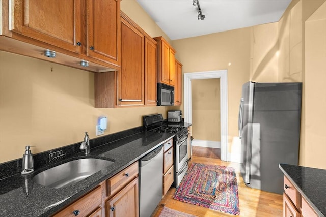 kitchen with brown cabinetry, light wood-style flooring, appliances with stainless steel finishes, dark stone countertops, and a sink