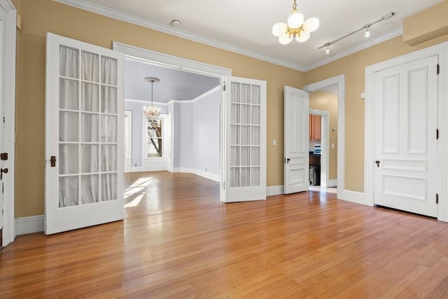 spare room featuring light wood-type flooring, crown molding, baseboards, and an inviting chandelier