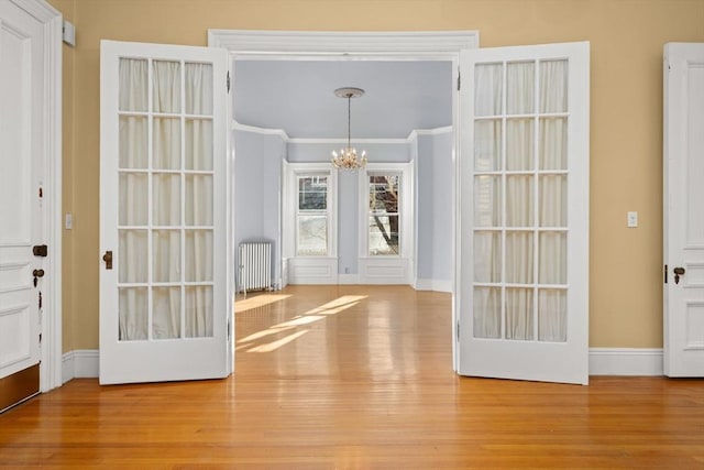 entryway with radiator, a notable chandelier, baseboards, and wood finished floors